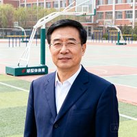 河北某中学校长王志明的正面半身照，他穿着深蓝色西装，背景为学校操场，该校使用了球探体育的校园体育器材配置